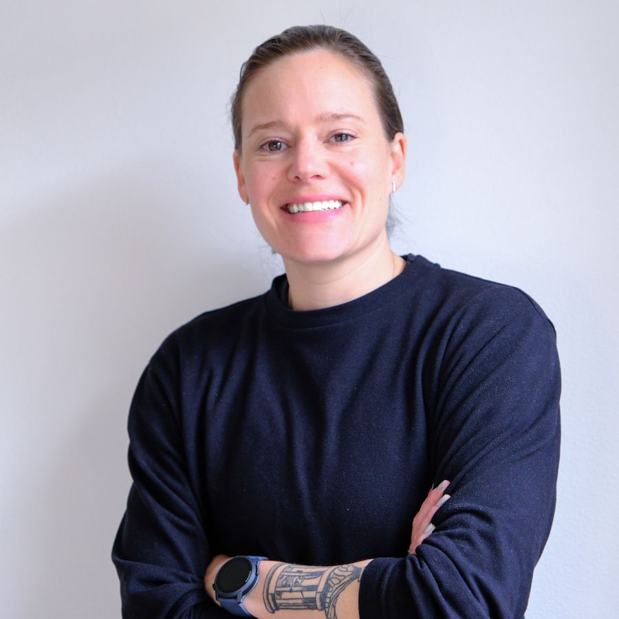 Anne-Marije Rook, smiling, arms crossed, in a navy sweater against a light wall