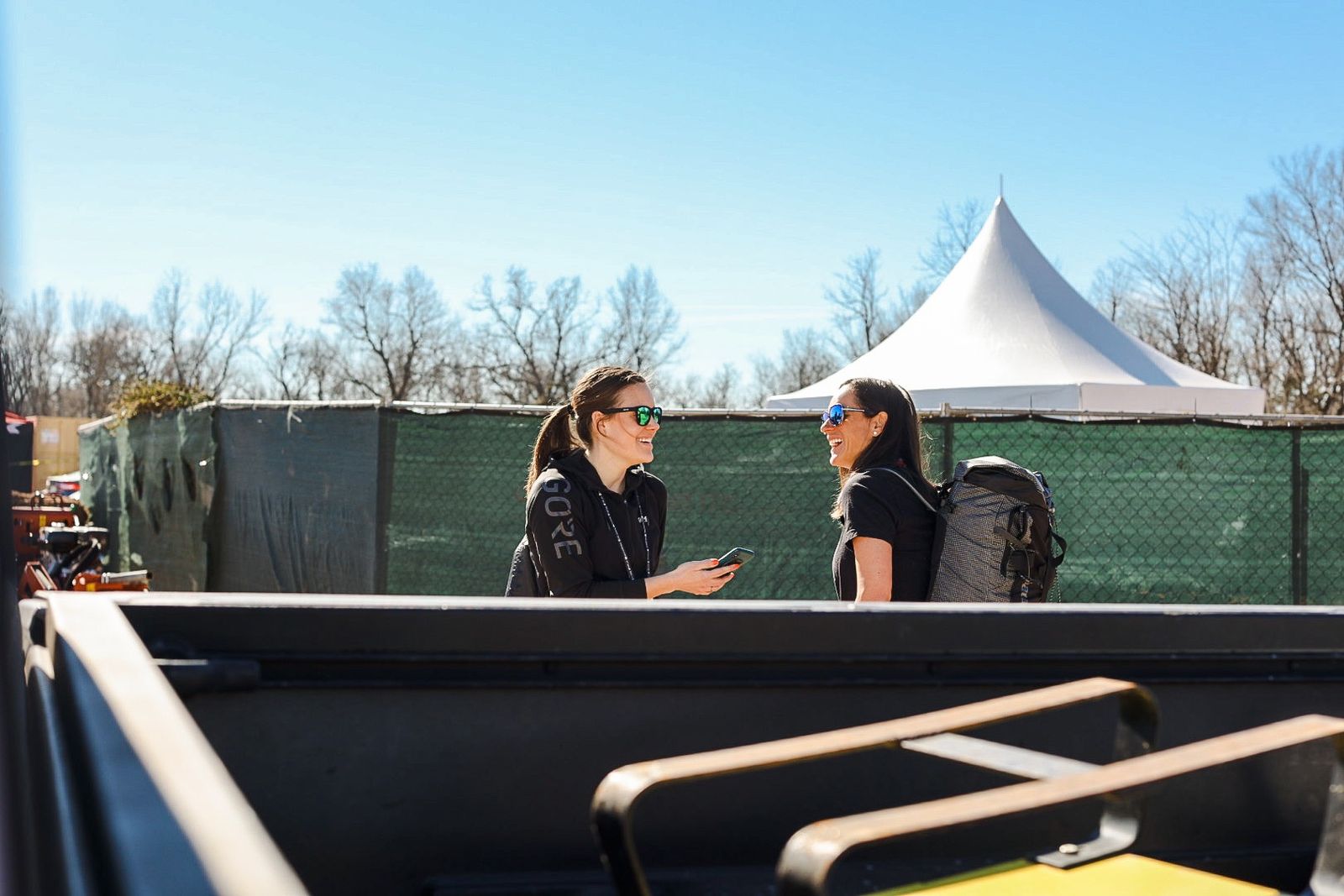 Anne-Marije Rook laughing with a rider while recording an interview on her phone at an outdoor race venue