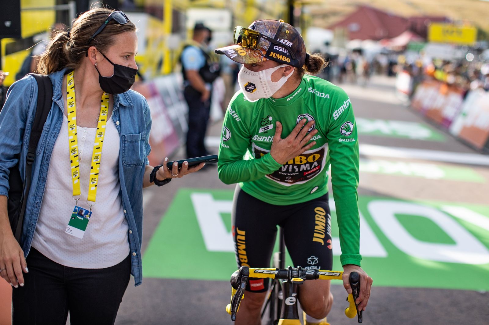 Anne-Marije Rook holding out a phone to record a post-race interview with a rider in the green jersey
